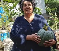 Mujer sonriente sosteniendo un zapallo de su huerta